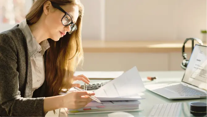 Frau geht vor einem Laptop Rechnungen und Unterlagen durch