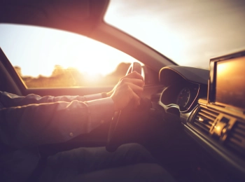 Person am Steuer eines Autos, von der Seite scheint die Sonne rein