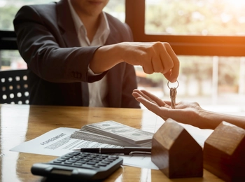 eine Person überreicht einer anderen Person die Schlüssel fürs Eigenheim