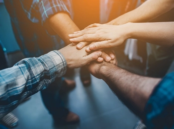 Hände treffen sich und werden in der Mitte aufeinander gelegt