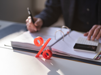 Ein Mann sitzt vor einem Ordner und rechnet, vor ihm steht ein rotes Prozent-Zeichen