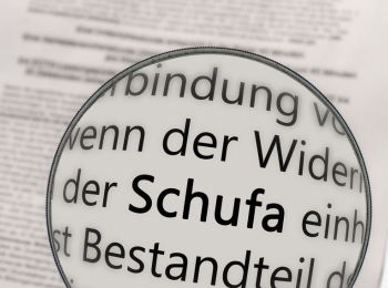 Lupe über einer Zeitung, der Begriff Schufa ist groß zu sehen