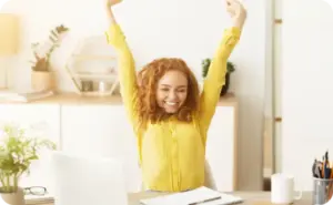 Frau am Schreibtisch reißt die Hände in die Luft und freut sich