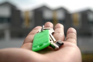 steigende Baustoffpreise - Hand mit Hausschlüssel, im Hintergrund verschwommende Silhouetten von Häusern