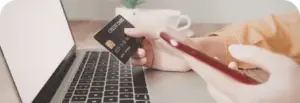 Person mit Handy und Kreditkarte vor dem Laptop
